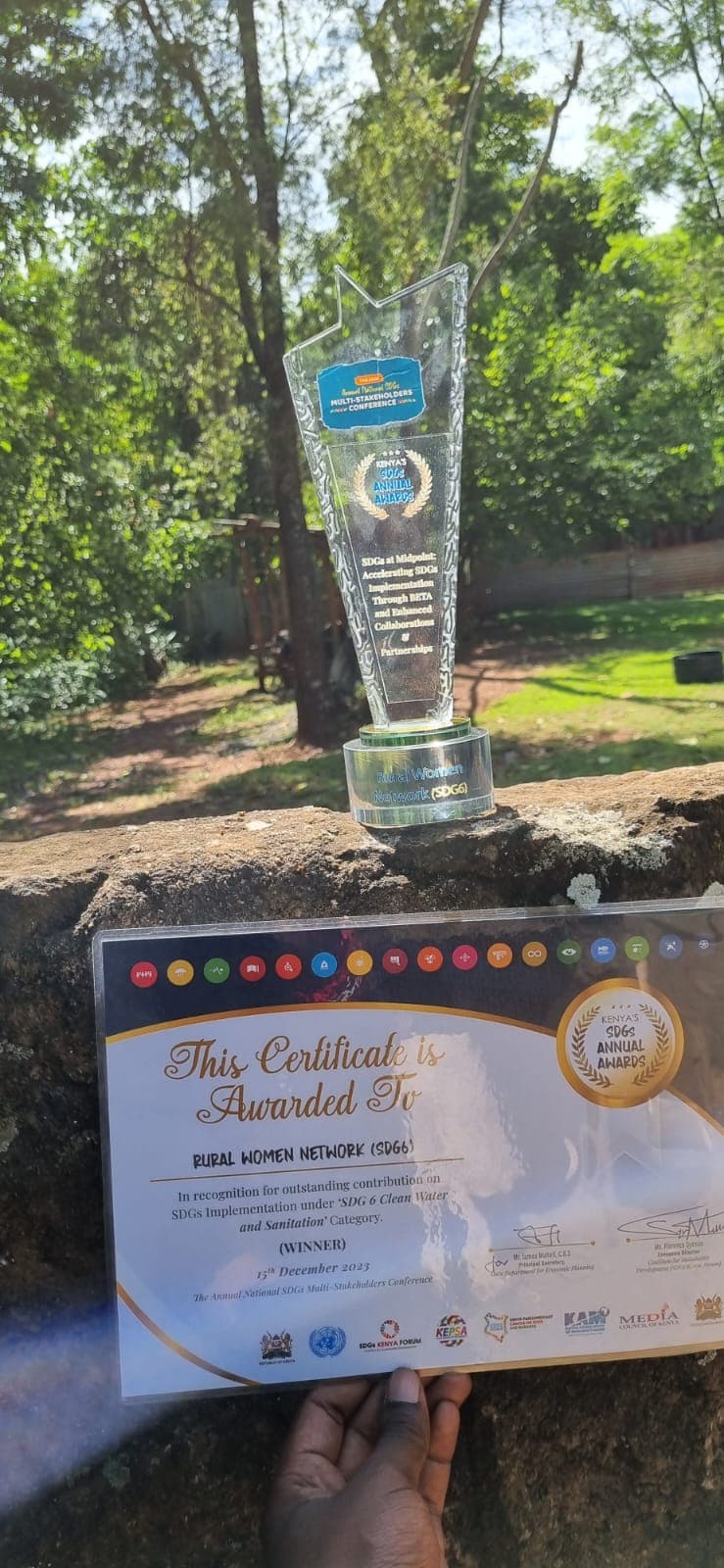 A hand holding the SDG 6 glass award beside its certificate